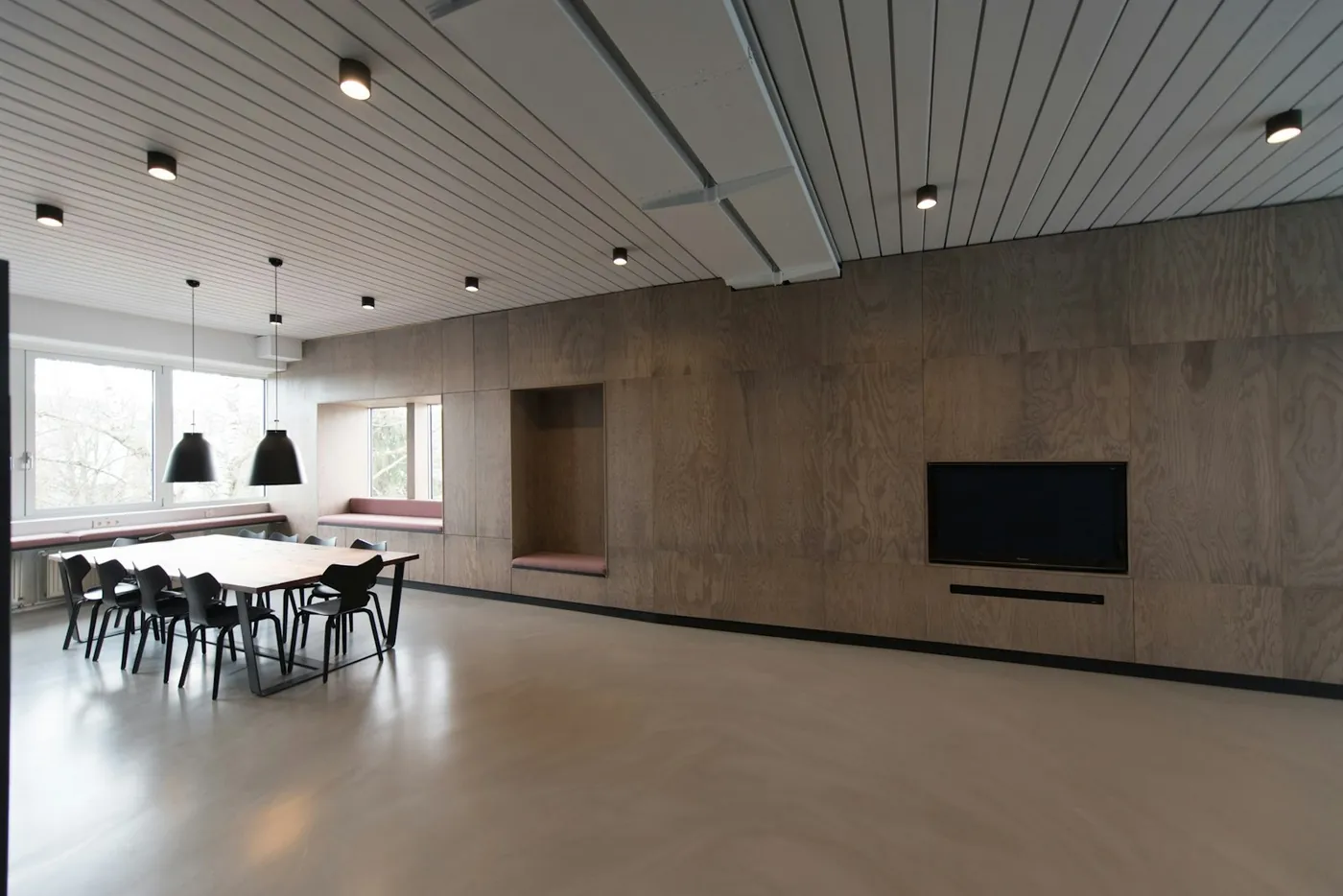 An empty meeting room with a long white table, black chairs and a dark timber wall running to a full-height window
